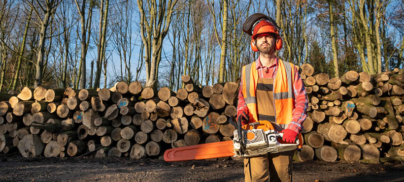 Forestry students standing with chainsaw in front of stacked fallen trees Forestry students standing with chainsaw in front of stacked fallen trees