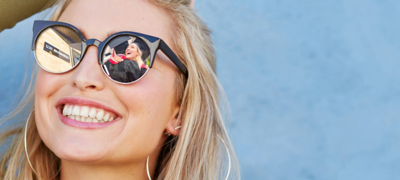 Woman smiling wearing sunglasses reflecting UHI Inverness campus building and graduates Woman smiling wearing sunglasses reflecting UHI Inverness campus building and graduates