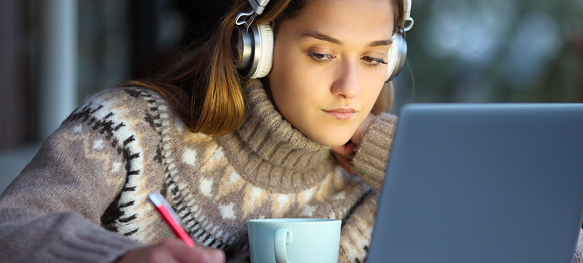 Student working on laptop at desk with headphones on Student working on laptop at desk with headphones on