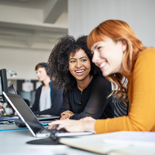 Two people smiling and using laptops