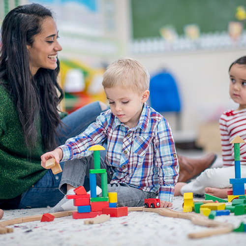 Two children and a person playing with wooden blocks