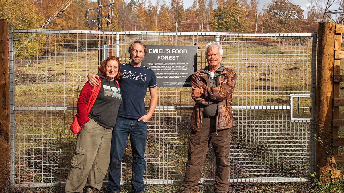 A woman and two men standing by a large field gate