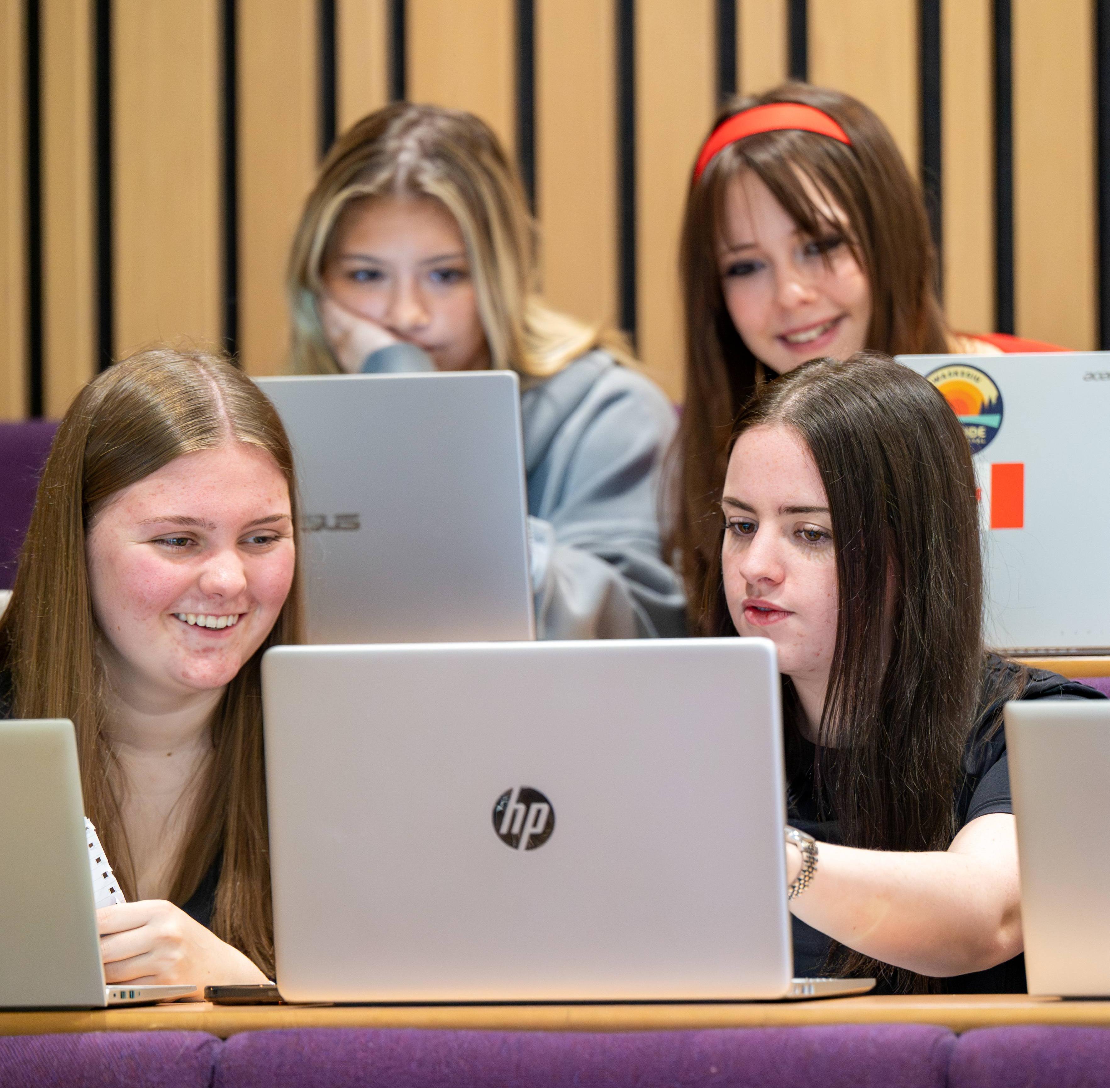 Four students looking at a laptop in a lecture theatre Four students looking at a laptop in a lecture theatre